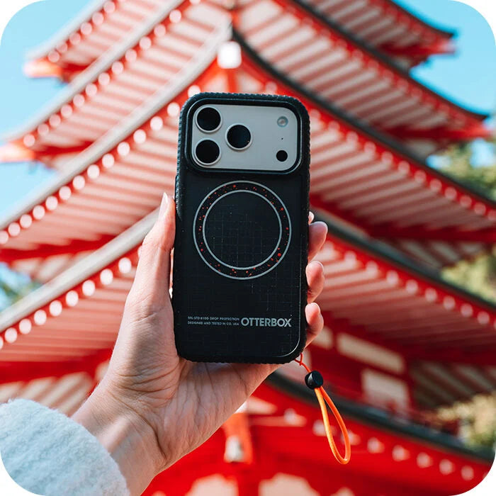 Person holding a black OtterBox phone case with a red traditional Japanese building in the background