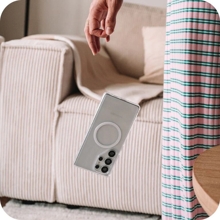 Smartphone being dropped in front of a beige sofa by a person wearing plaid pajama bottoms.