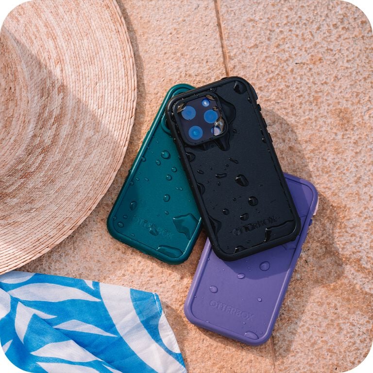 Three phone cases in teal, black, and purple on a textured surface with a hat and towel.