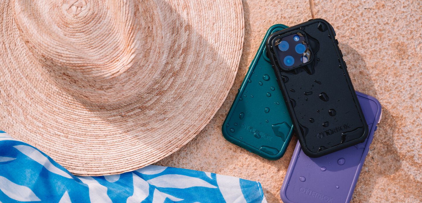 Three phone cases in teal, black, and purple on a textured surface with a hat and towel.