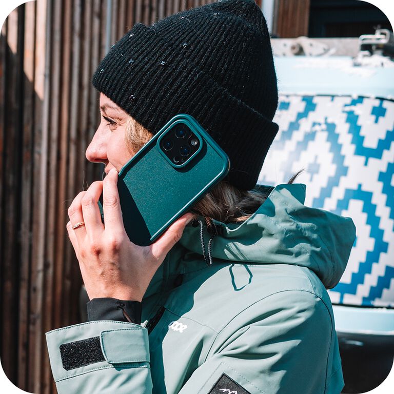 Person talking on a phone with a teal case, standing next to a van with a geometric pattern.